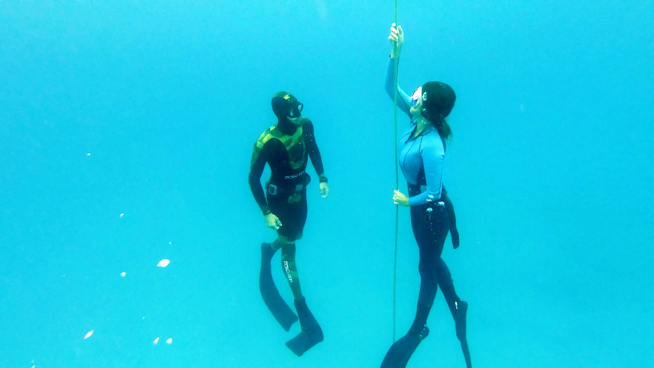 Two freedivers along the line in turquoise water, one holding the rope.