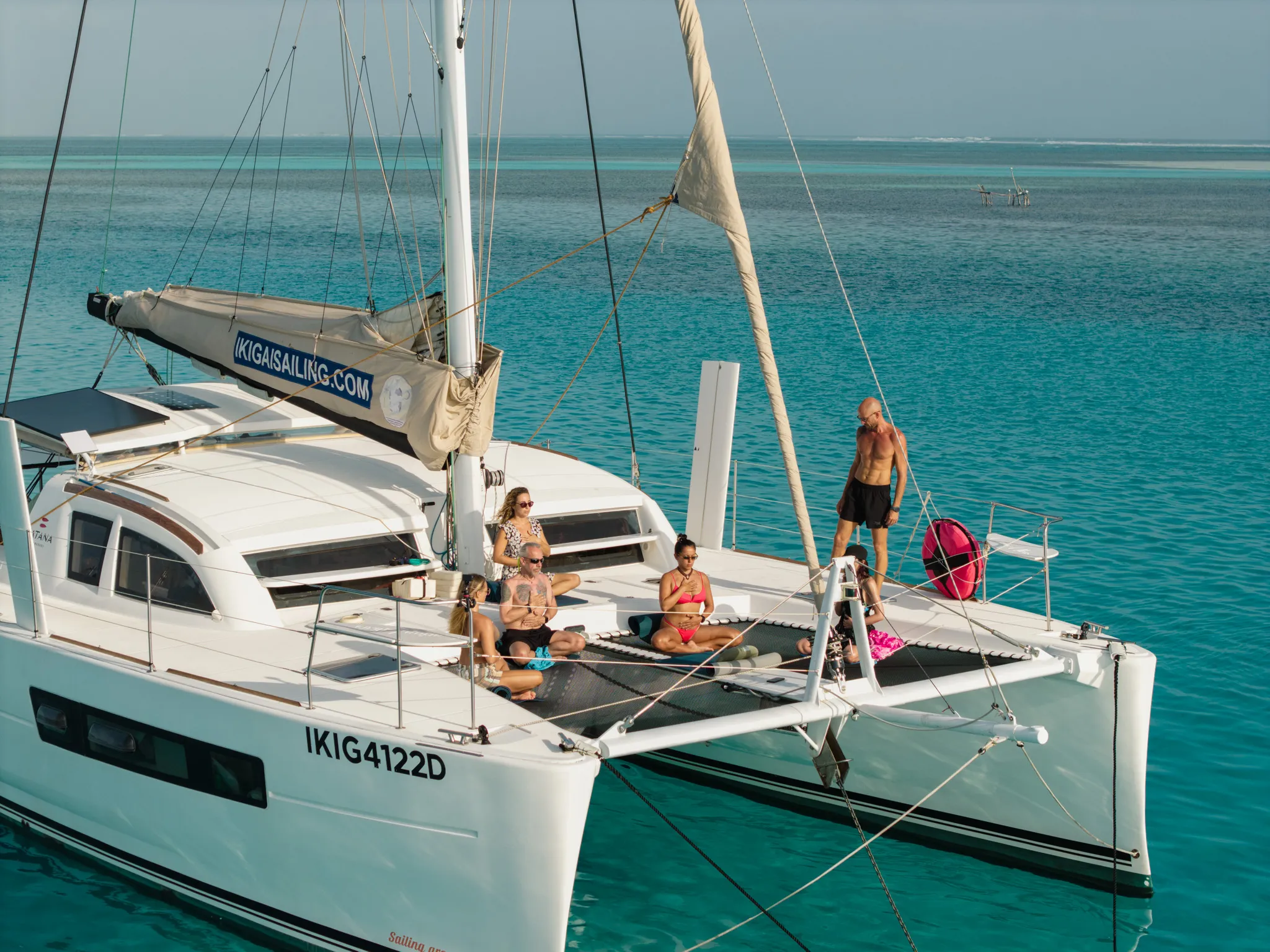 Guests sitting in meditation on the catamaran’s bow trampoline, at anchor.