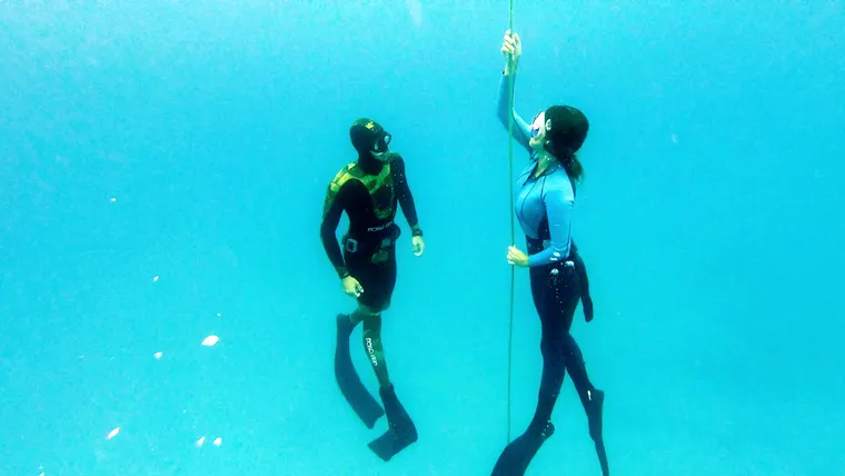 Two freedivers at the line in clear turquoise water, one giving the OK sign.