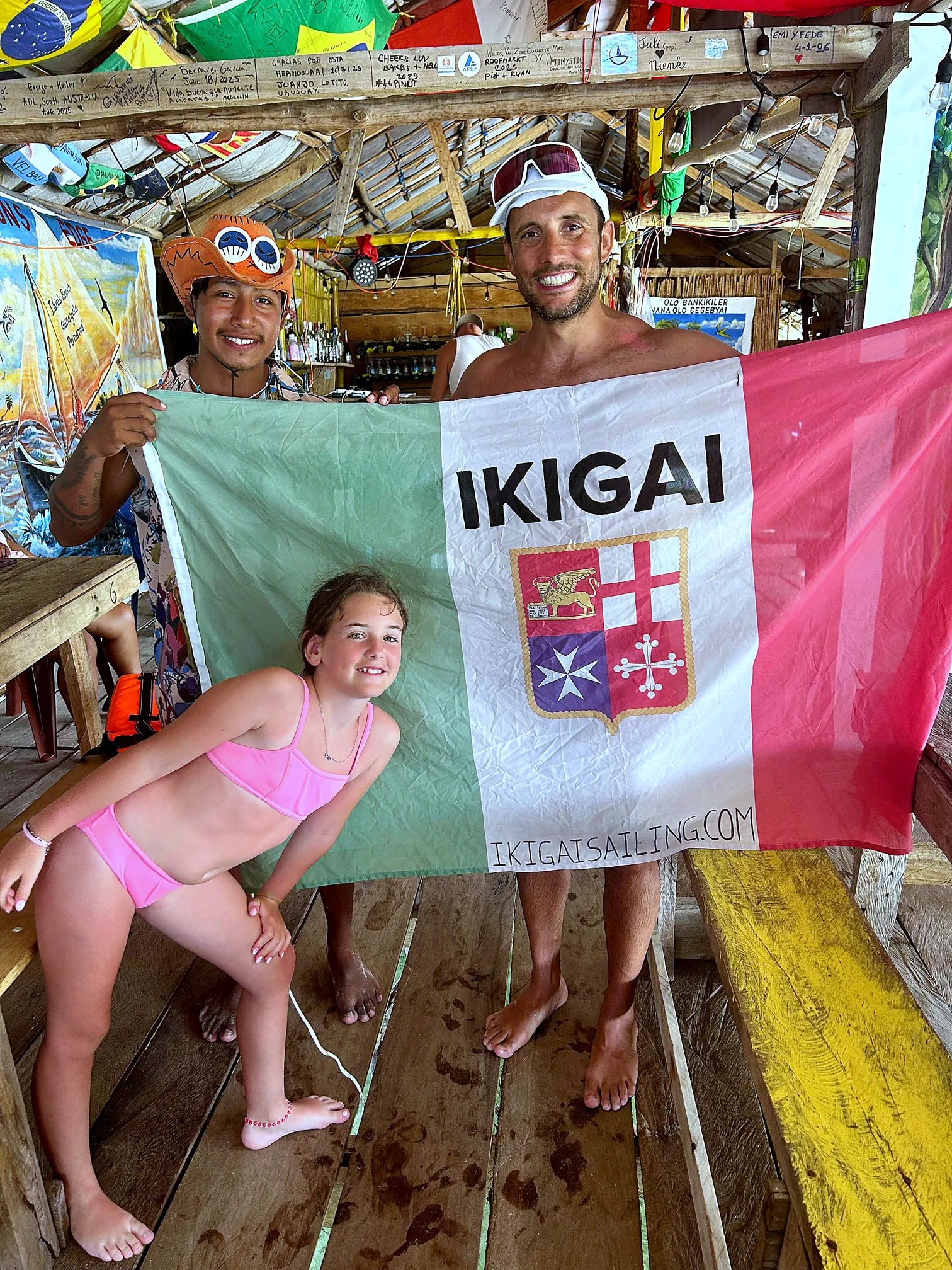 Luca holding the IKIGAI flag in a Guna bar, with a friend and a little girl